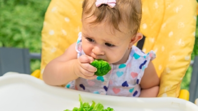bébé qui mange un légume vert type brocoli